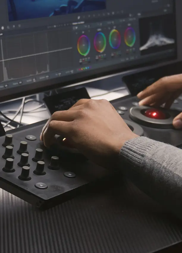 Le mani di una persona azionano un pannello di controllo per la gradazione del colore davanti a un monitor che visualizza strumenti di correzione del colore, software di editing video e riprese di cantieri in timelapse. video timelapse